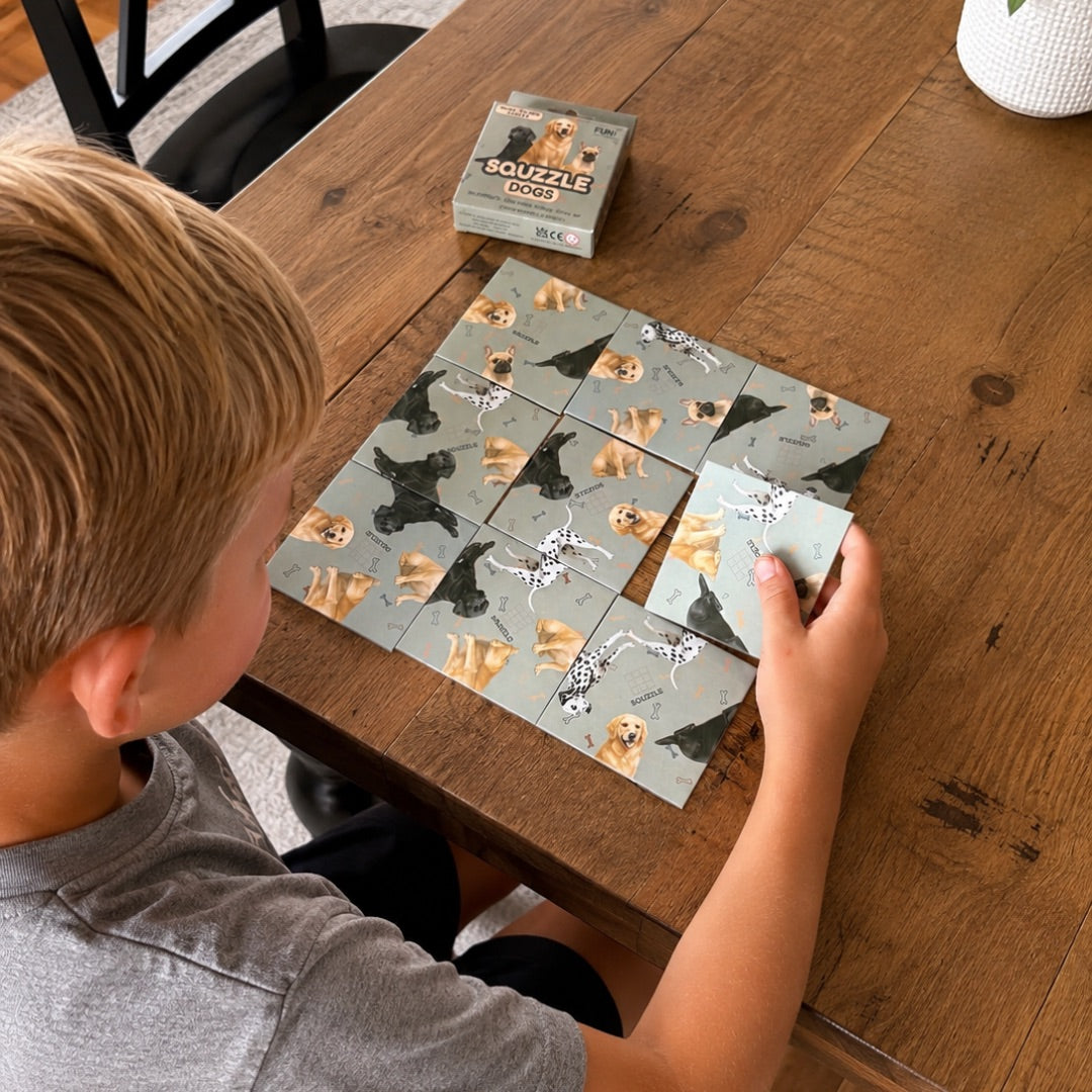 A person arranging nine Dogs Squzzle picture tiles at a table, with the matching box nearby.