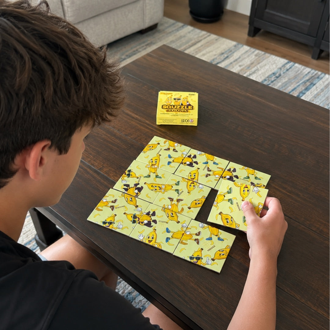 A person arranging nine Bananas Squzzle picture tiles at a table, with the matching box nearby.