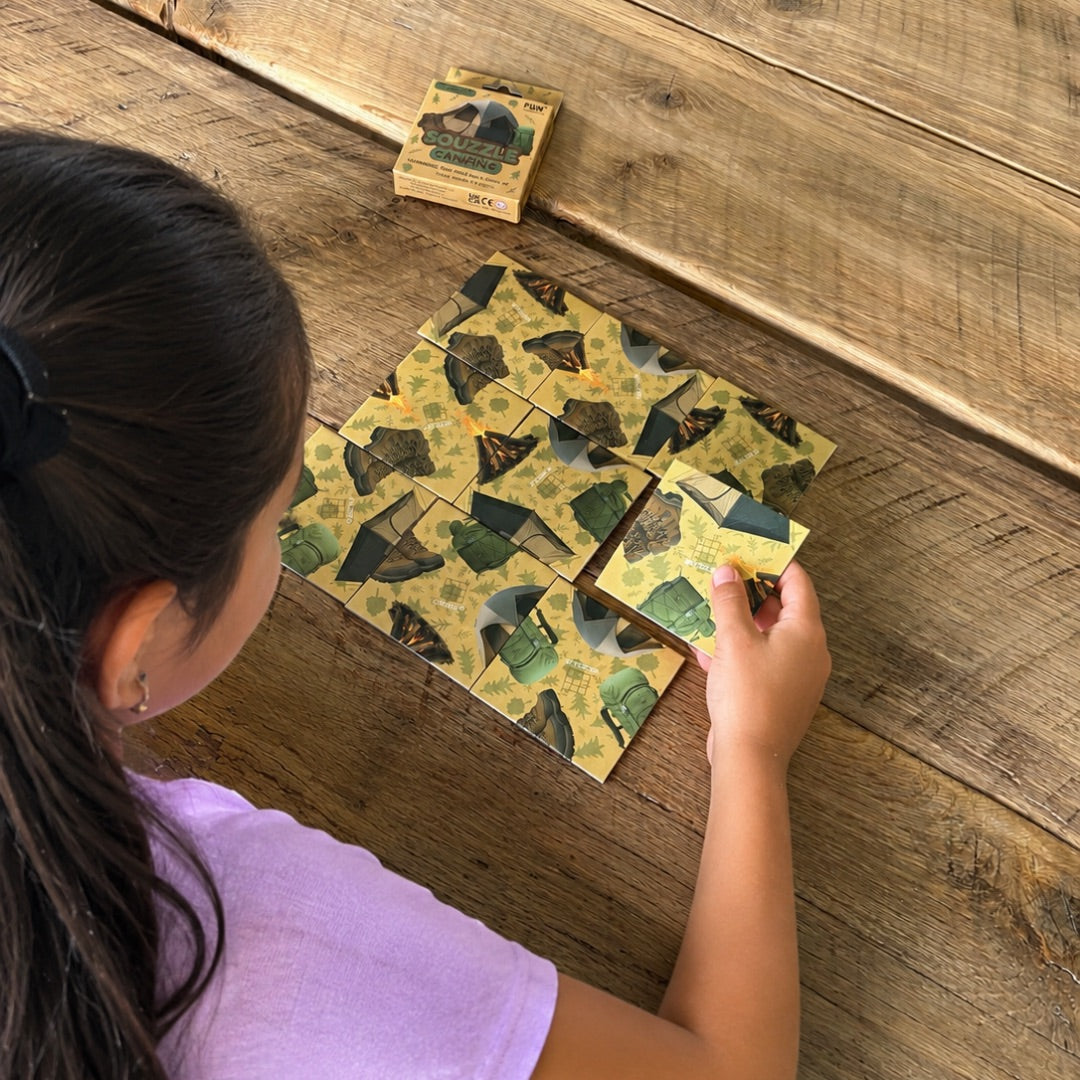 A person arranging nine Camping Squzzle picture tiles at a table, with the matching box nearby.