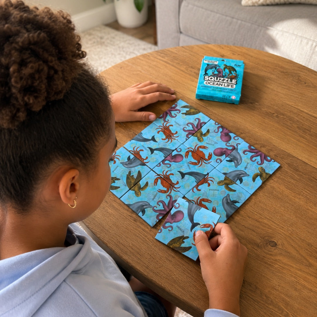 A person arranging nine Ocean Life Squzzle picture tiles at a table, with the matching box nearby.